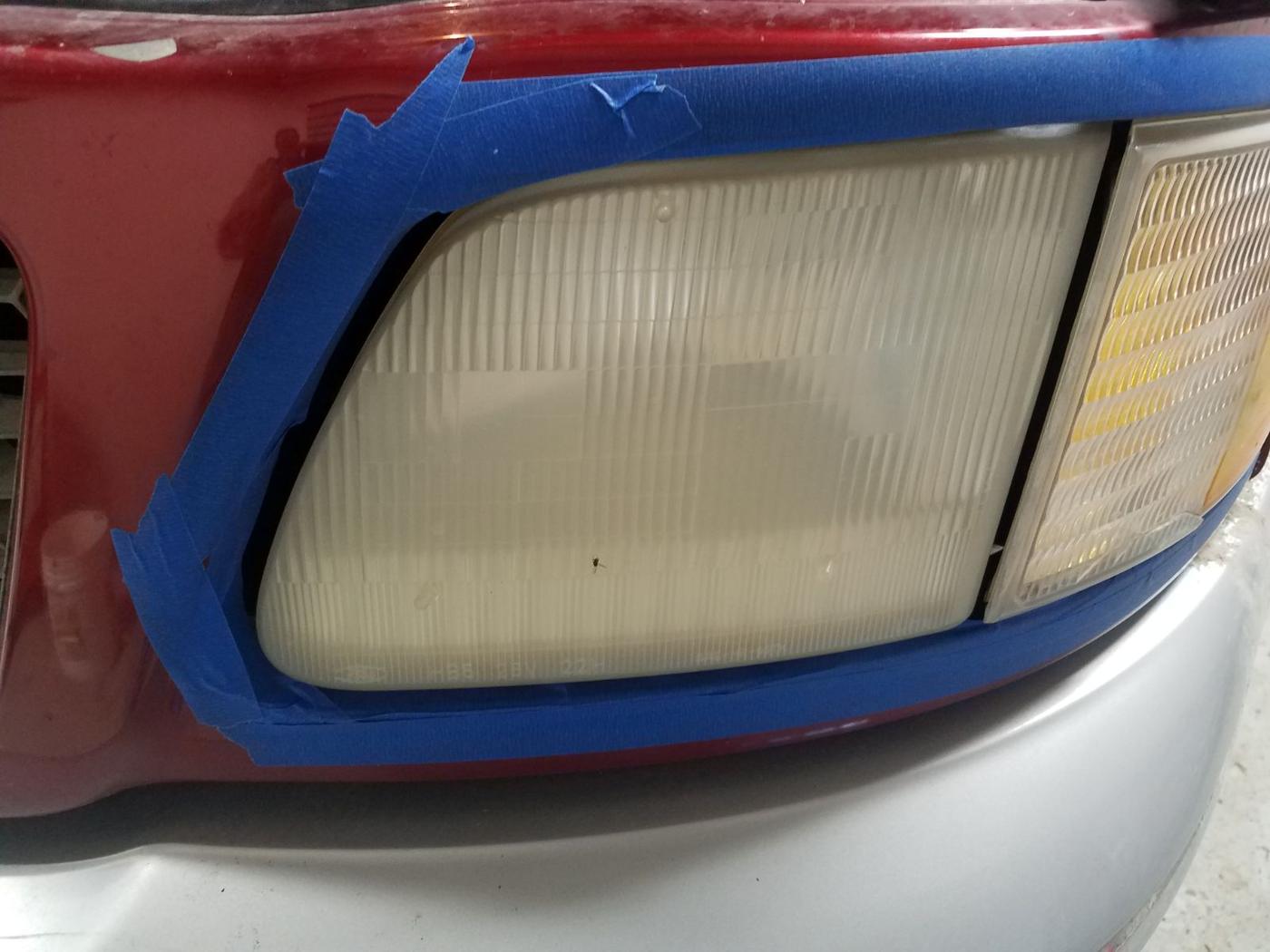 Hazy truck headlight masked off with blue tape, mid restoration